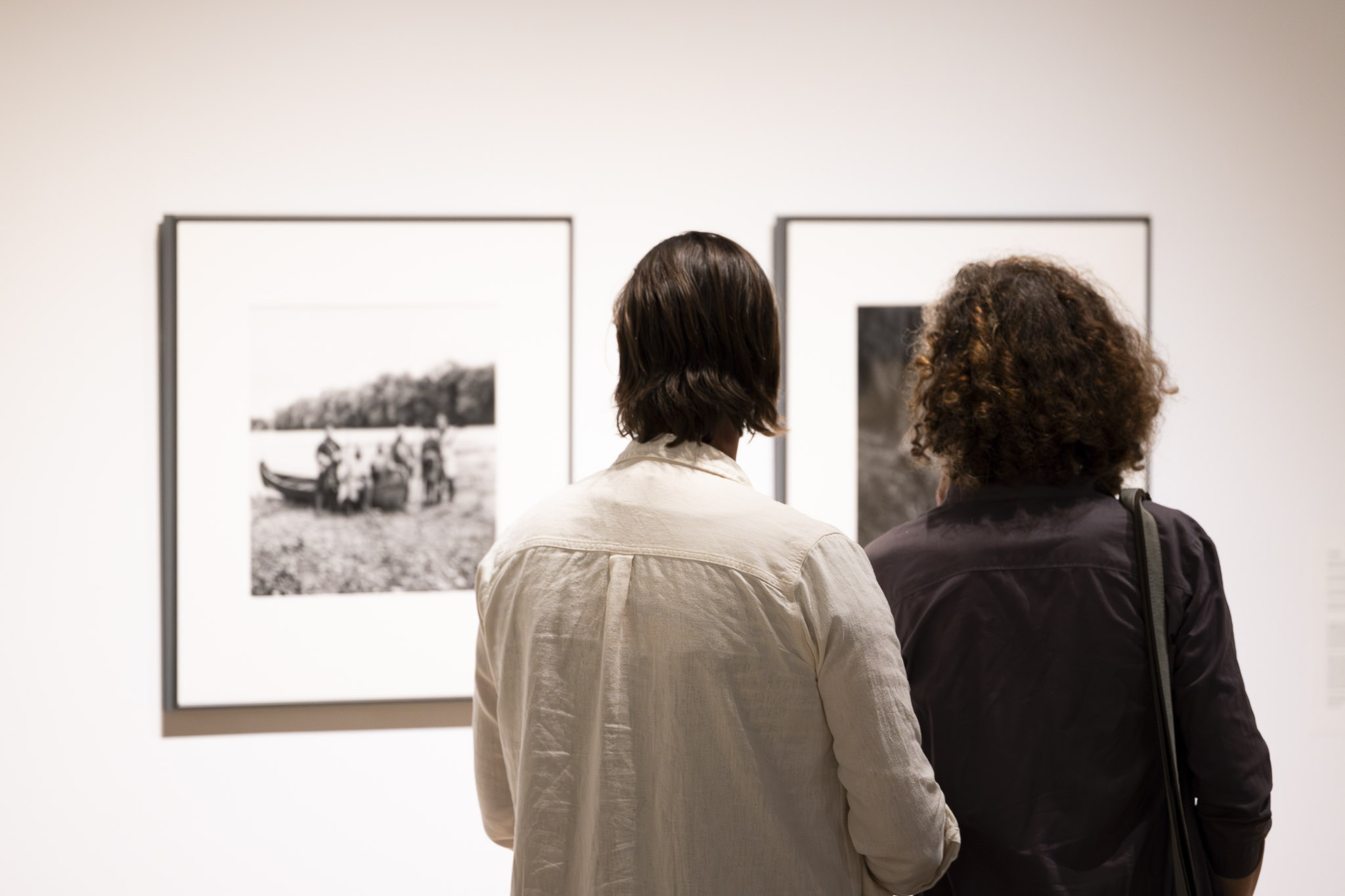 Two people viewing black and white photographs in a gallery. Their backs are to the camera