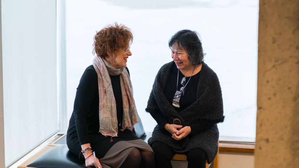 curator Lori Beavis and artist Shelley Niro smiling and laughing, engaged in a conversation at the Art Gallery of Peterborough