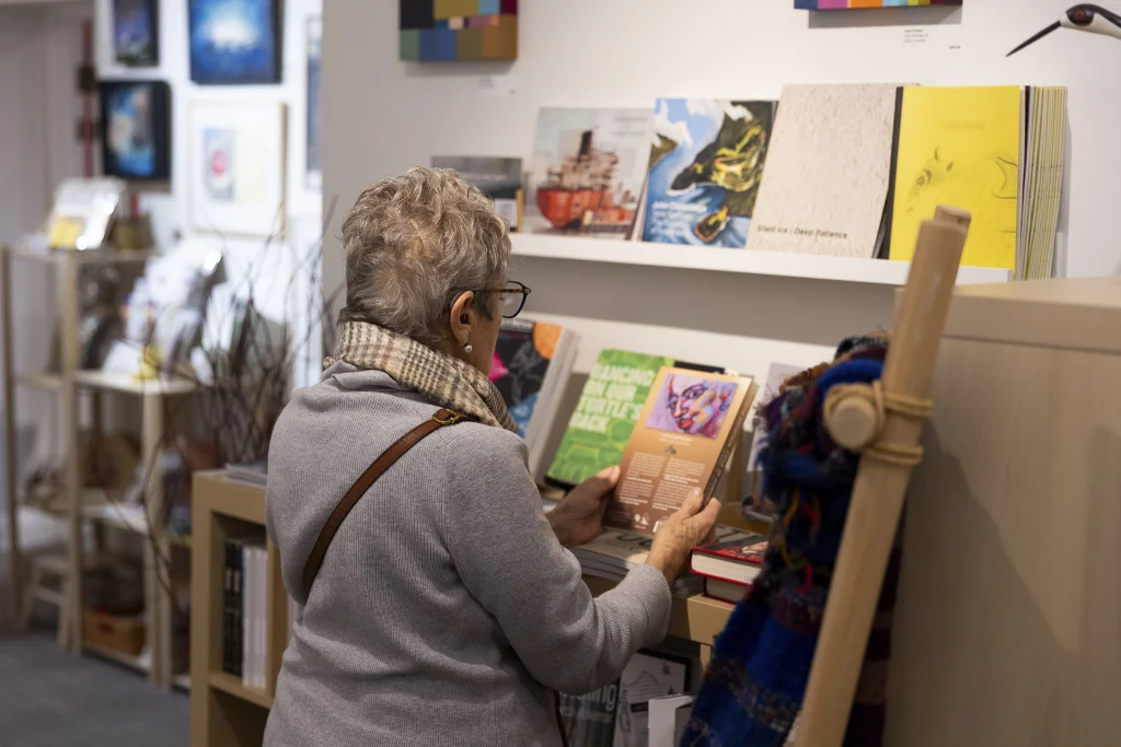 a person holds up a book to read the back cover in the AGP gallery shop