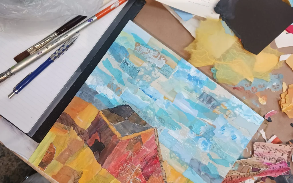 mixed media collage of a red barn in a golden field sitting on a desk with art supplies
