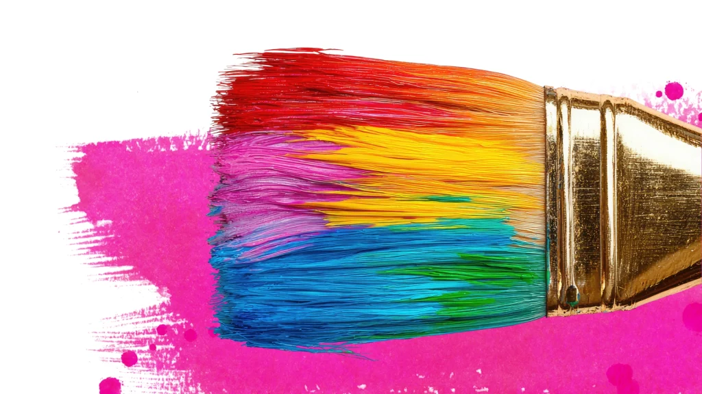A golden paintbrush with vibrant red, orange, yellow, green, and blue bristles paints a bright pink streak on a white background, conveying creativity.