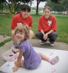 Two volunteers with a child drawing outside during an AGP summer art camp