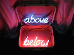 Sculpture by Orest Tataryn featuring an open suitcase with two red and blue neon lights. Text reads: "Above Below."