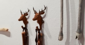 Walking sticks by Barbara Lounder installed in AGP's main gallery. Two dear head hooks holding two brown wooden walking sticks. Two grey wooden walking sticks with hooves.