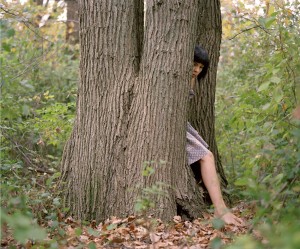Photograph by Melissa General. Person steping out from behind a tree in a forrest.