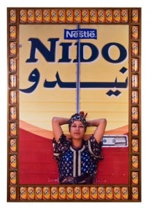 Photograph by Hassan Hajjaj. Person standing in front of a van with the text "Nestle Nido." Photograph is framed by orange Nestle Nido cans.