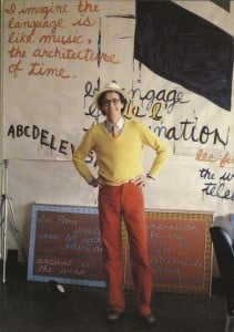Dennis Tourbin standing in front of a large text based painting in his studio