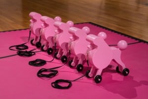 Sculpture by Mary Anne Barkhouse installed in the AGP's main gallery. Five pink wooden poodles on pink and black play foam tiles.