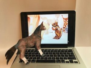Three dimensional paper collage of a brown horse standing on a laptop keyboard with a brown and white chipmunk on the screen