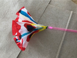 Paper flower dyed with red, blue, and yellow watercolour. Pink straw as a stem.