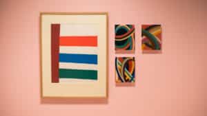 Abstract painting by Jack Bush featuring four red, blue, and brown block lines on a white background. Three digital drawings installed as chromogenic prints mounted on plexiglass by Francisco-Fernando Granados. Bright red, blue, green, yellow, brown, and black block lines, straight and curved.