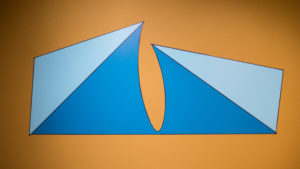 Digital drawing of a light and dark blue stylized ice-berg form by Francisco-Fernando Granados installed as vinyl on a yellow wall in the AGP's main gallery