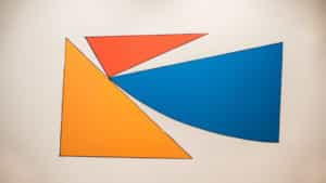 Digital drawing by Francisco-Fernando Granados installed as vinyl on a white wall in the AGP's main gallery. Red, blue, and yellow two dimensional triangles, various sizes.