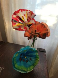 Three paper flowers dyed with green, blue, red, and orange watercolour in a vase on a table