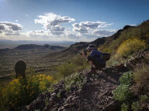 Corin Ford Forrester crouched on a hill taking a photograph of a cactus
