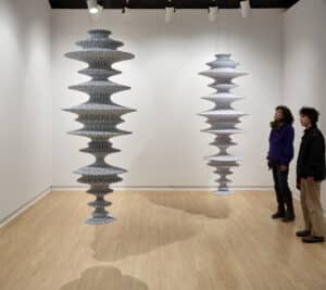 Two people looking at Lyn Carter's two hanging cylindrical sculptures with black and white skins installed in the AGP's main gallery