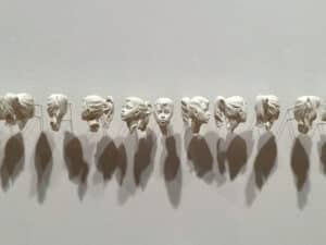 Marble dust sculpture by lo scott. A sequence of small female heads attached to a wall with hydrocal steel.