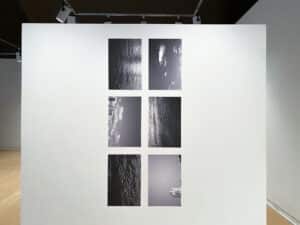 Gallery view of the exhibition Presently featuring Nadja Pelkey's grid of six black and white photo prints of Windsor and Detroit turned sideways installed in AGP's main gallery