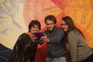 Three people taking a selfie in front of an acrylic painting installed in the AGP's main gallery