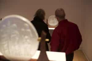 Two people looking at a glass sculpture on a plinth installed in the AGP's main gallery