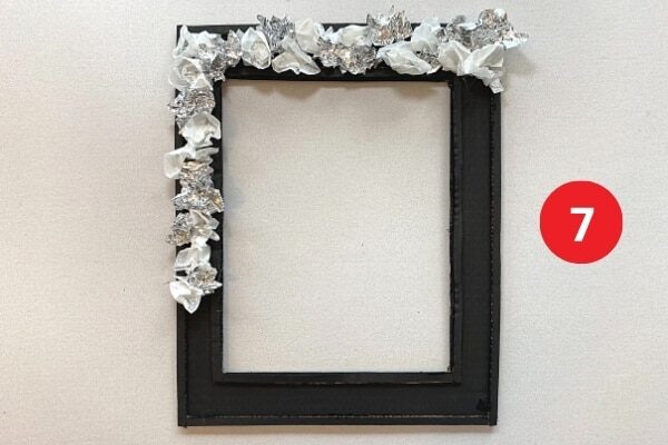 Tinfoil and papers flowers glued to a black rectangular cardboard frame. Text reads "7."
