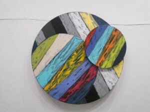 Circle made of planks of colourful painted wood with another moveable circle attached on the right by Stan Olthuis