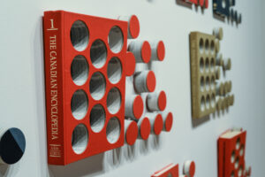 side view of installation artwork featuring a Canadian Encyclopedia with circular holes cut out. The cut outs are arranged in patterns beside the book.