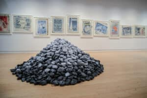 pile of paper rocks in foreground with a gallery wall of framed, enlarged stamps in the background