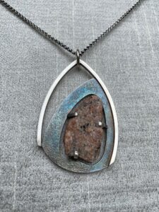 A necklace with a silver frame holding a stone at an asymmetrical angle.