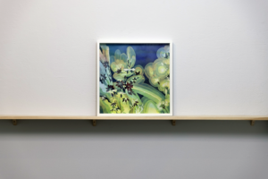 A Painting of flowers with warm gradations and a blue background. Painting is framed sitting on a pine shelf.