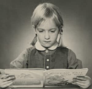 black and white photo of Michèle Karch-Ackerman as a child reading a book