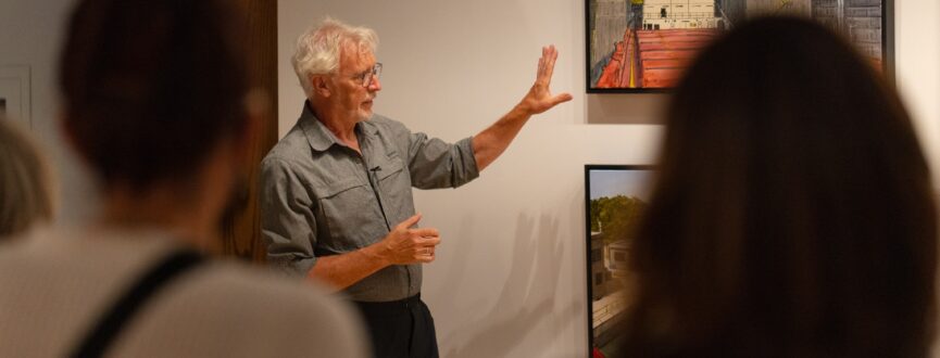 Peer Christensen delivering an artist talk and pointing to one of his paintings on the wall.