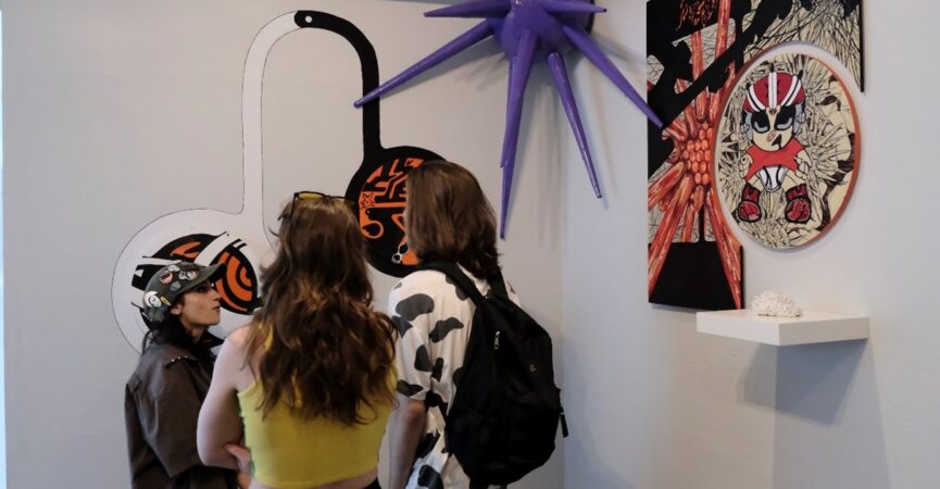 Three youth standing in the exhibition discussing the artwork