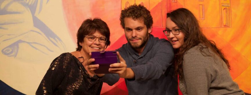 Bonnie Devine takes a selfie with two people in front of a painting