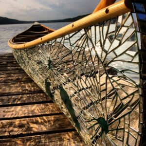 a green canoe with a mirror mosaic on the surface sits on a wooden dock with a body of water behind