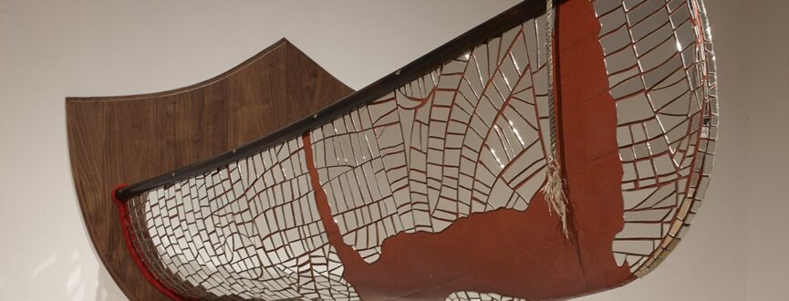 installation artwork of a rust coloured canoe with mirrored mosaic patterning cut in half and mounted on a wooden plaque that has been installed on a gallery wall