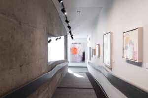 abstract artworks by Carol Forbes hang in a gallery space featuring concrete walkways and grey handrails extending downward