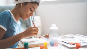 A teenager paints on a canvas in a studio