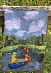 A felted textile of a landscape scene in an impressionist style. The scene features two canoes on the water with a red canoe in the distance, and a blue canoe in the foreground, the figures are wearing yellow life jackets and hats. The landscape is lush with shades of green under a blue sky with white clouds.