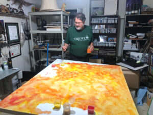 David Beaucage Johnson paints in his studio with watercolour on a canvas laid flat in the foreground.