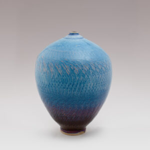 A vessel that is narrow at the top and bottom. The blue colour is pattered with artist markings and becomes more of a gradient into a dark purple at the bottom.