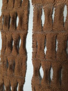 Copper wire weaved into a quilt-like pattern, the woven strips are in sections that contain about four vertical strips and they have negative space between each section.