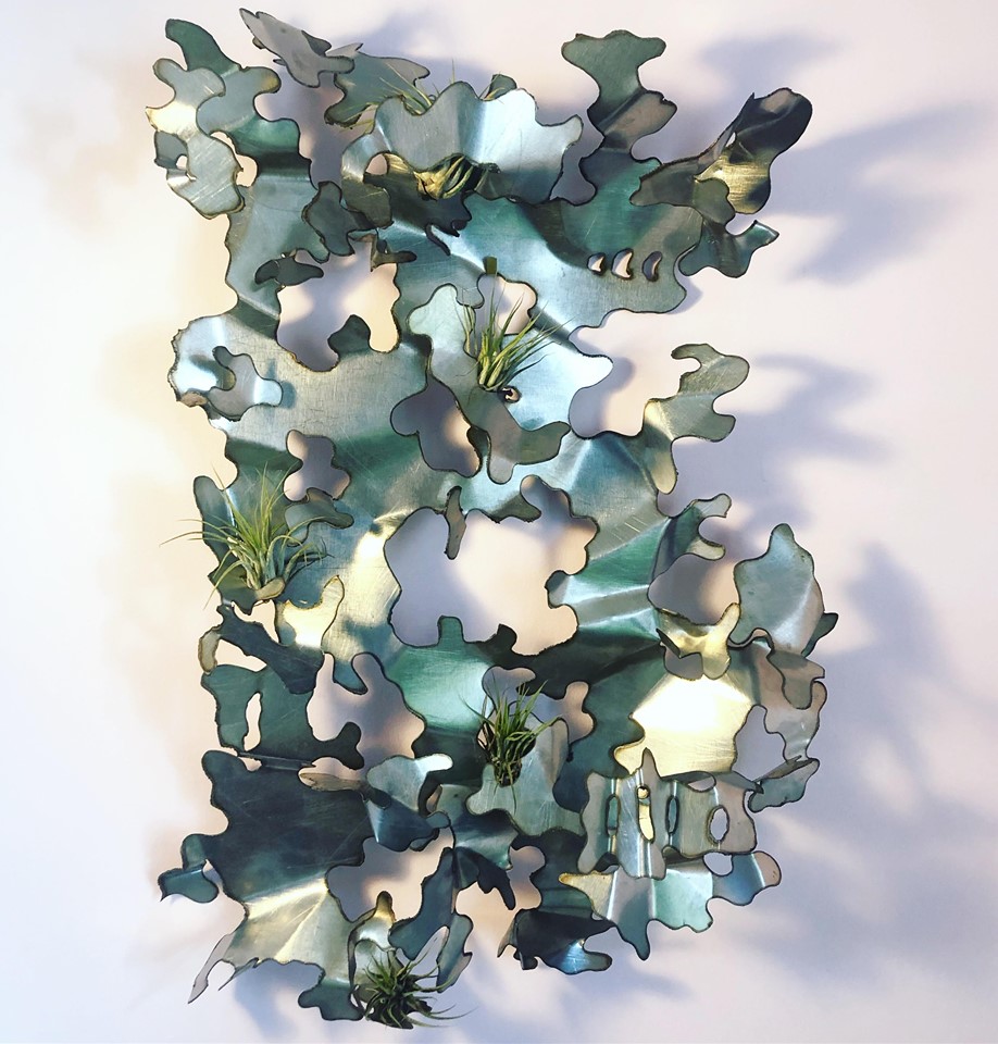 Green and silver metal sculpture with irregular edges, folds, and cuts. Air plants are incorporated into some folds.
