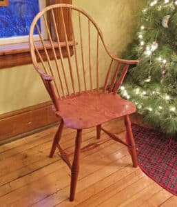 A wooden chair with an arched back, spindles, and arm rests. The warm stain brings out the grain of the wood.