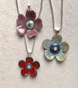 Three flower pendants: pink, green and red with five pedals each, displayed on chains on a white background.