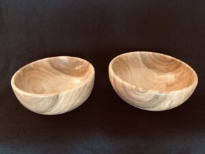 Two light wooden bowls with a distinctive grain set on a dark background.